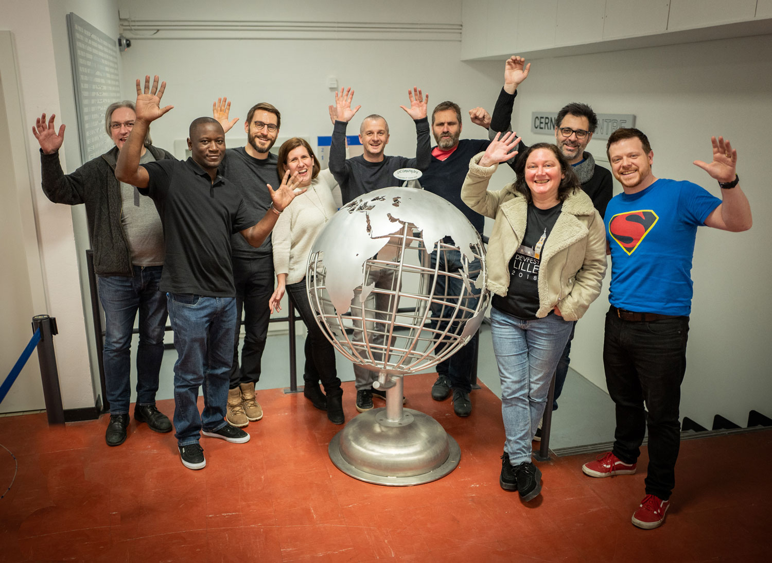 The team gathered around a globe in the basement of the CERN Data Centre. They’re smiling and their arms are raised in celebration.